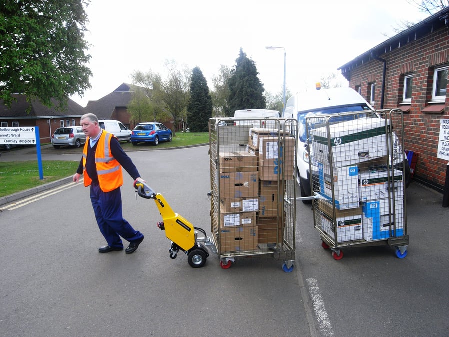 Employee moves roll cages with help from electric tug