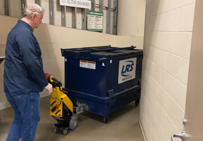 janitor moving heavy dumpster in trash room