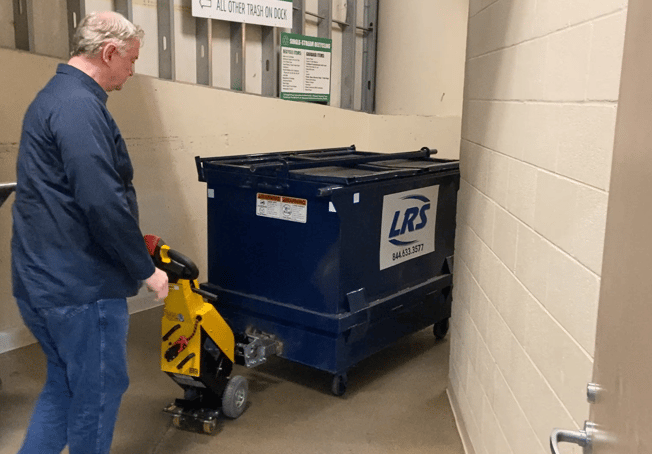 janitor moving heavy dumpster in trash room