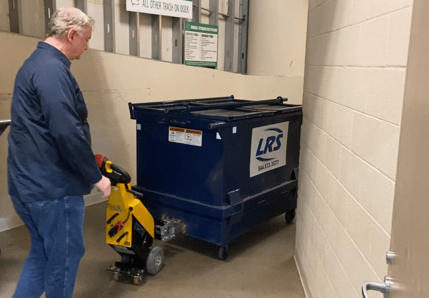 janitor moving heavy dumpster in trash room